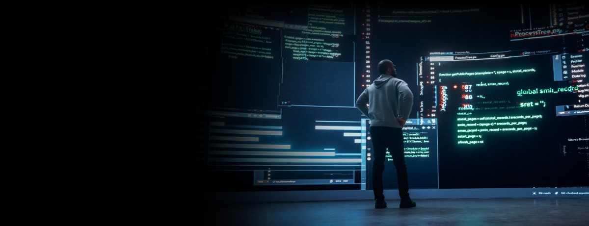 man standing in front of giant monitors running code