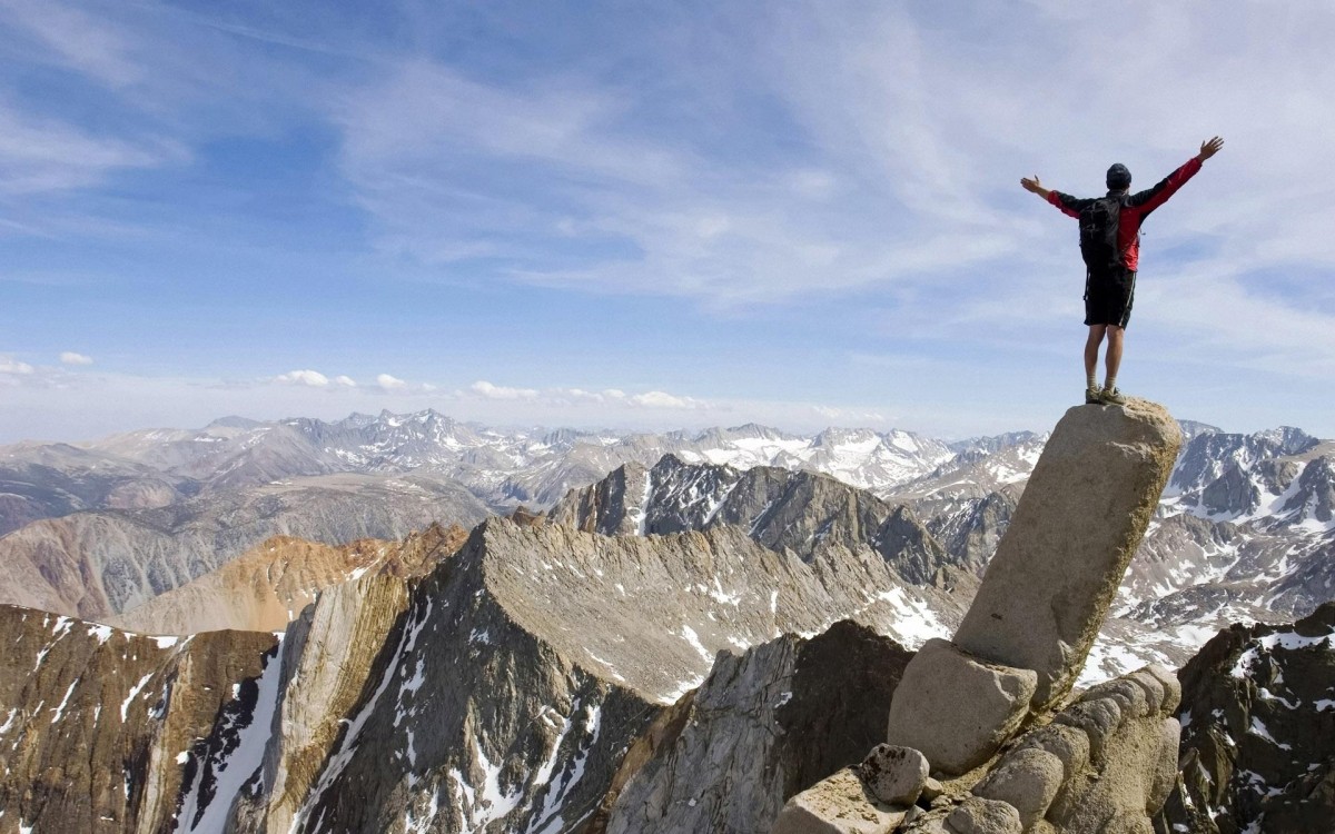 Man standing with arms outstretched on top of mountains