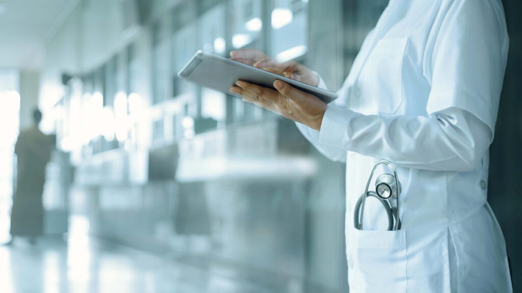 Doctor standing in a hospital corridor, tapping on an ipad